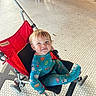 toddler, child, stroller, red_stroller, space_onesie, smiling, indoor, tile_floor, legs, shoes, candid, playful, baby, person, seat, wheel, footwear, casual, happy, portrait