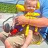 baby, child, life_jacket, earmuffs, adult, boat, water_plants, sky, blue_shirt, shorts, summer, outdoor, sunlight, person, nature, greenery, smile, hair_spikes, safety, holding