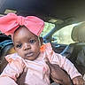 Justice is registered to the contest to win money with this photo: baby, child, pink_bow, indoor, car_interior, person, cute, infant, clothing, hands, portrait, seat, window, soft_light, headwear, sitting, expression, young_child, human, skin