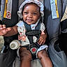 baby, car_seat, smiling, hat, dress, bottle, child, infant, safety_harness, happy, skin, hand, foot, indoors, person, seat, straps, cute, young, childcare
