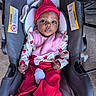 baby, infant, car_seat, red_hat, pink_bib, red_pants, bare_feet, looking_at_camera, indoor, warning_labels, clothing, child, person, seat, padding, cute, small_hands, wide_eyes, colorful_outfit, cozy