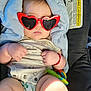 baby, child, sunglasses, heart_shaped, red, blanket, car_seat, toy, bracelet, clothing, infant, cute, closeup, indoor, accessory, person, skin, hand, legs, head