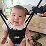 baby, jolly_jumper, indoor, smiling, child, suspended, floor, couch, toy, slippers, arm, face, person, tiled_floor, clothing, bracelet, happy, living_room, infant, playtime