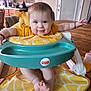 baby, infant, smiling, highchair, fisher_price, giraffe_pattern, yellow_clothing, baby_seat, table, kitchen, wooden_table, bottle, foot, hand, face, child, indoor, furniture, happy, cute