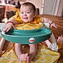 baby, child, smiling, yellow_clothing, walker, fisher_price, indoor, table, wooden_floor, happy, infant, face, arms, legs, toy, feeding_bottle, red_bracelet, home, cute, playful