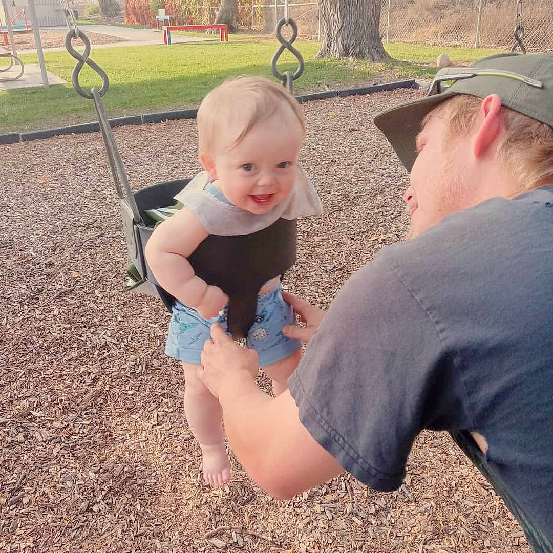 Lyric is registered to the contest to win money with this photo: asphalt, baby, baseball_cap, child, fun, gesture, grass, happy, hat, interaction, lawn, leisure, people_in_nature, person, plant, recreation, swing, t_shirt, thumb, toddler