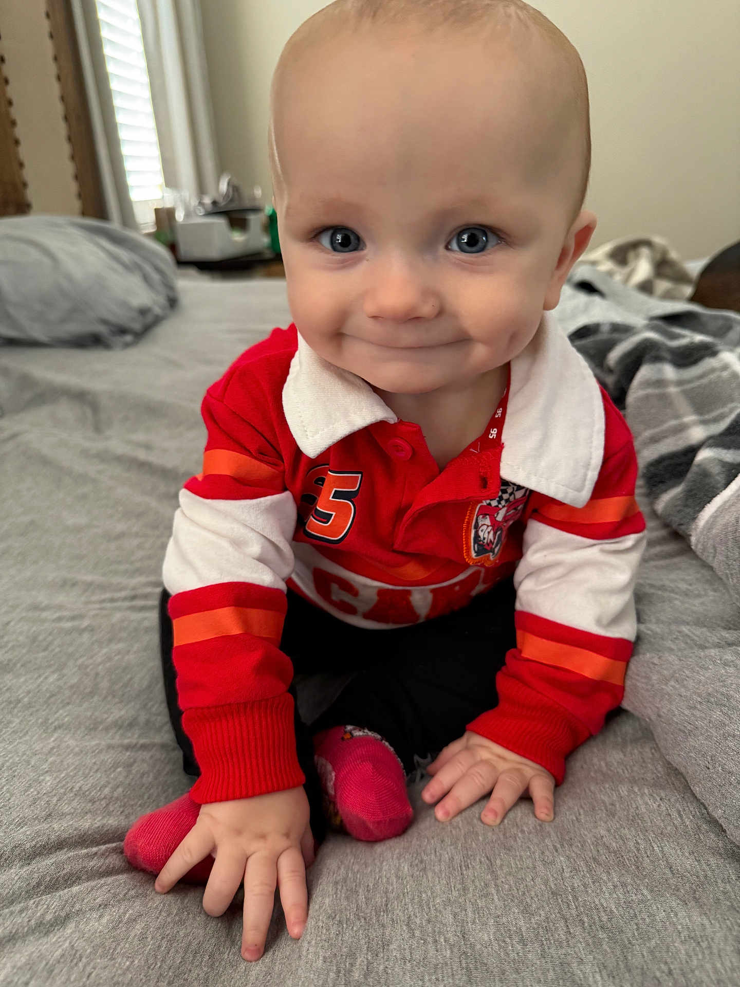 Stetson is registered to the contest to win money with this photo: baby, child, smiling, blue_eyes, dimples, red_shirt, long_sleeves, sitting, bed, blanket, pillow, indoor, hands, cute, infant, portrait, clothing, person, happy, crawling