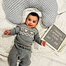 baby, infant, child, smiling, gray_clothing, knitwear, polka_dot_pillow, white_blanket, letter_board, milestone, portrait, cute, lying_down, cozy, happy, indoors, soft_texture, warm, childhood, baby_photography