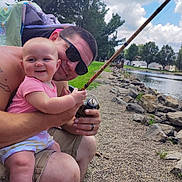 Carlie joined the competition — help win amazing prizes! baby, man, fishing_rod, lake, rocks, trees, outdoor, smiling, sunglasses, grass, clouds, water, fishing, child, happy, nature, summer, people, parent, recreation