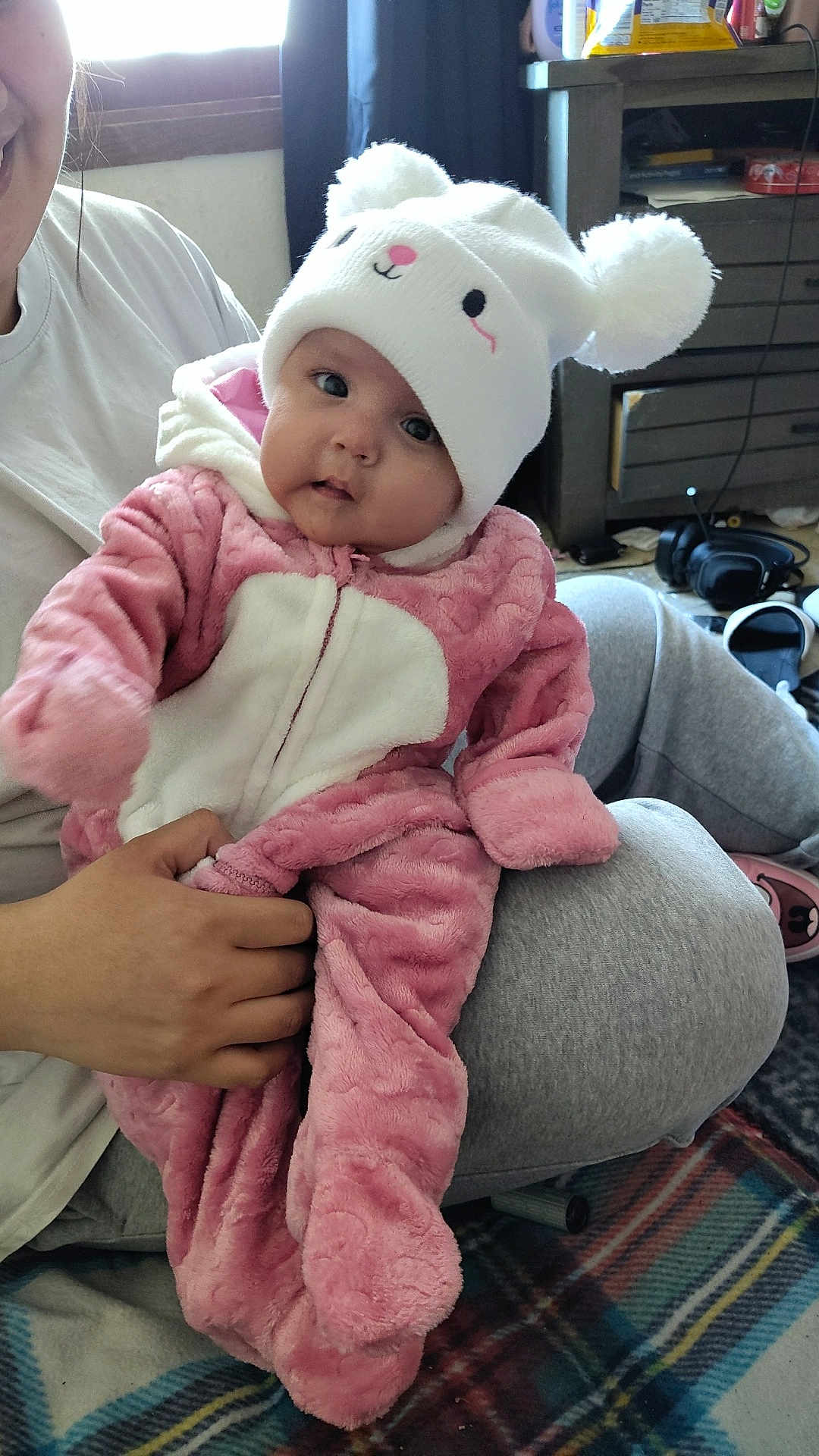 Maylynn Jo joined the competition — help win amazing prizes! baby, child, infant, pink_outfit, white_hat, pom_poms, cute, smiling, indoor, plaid_blanket, person, hand, face, clothing, cozy, floor, furniture, window, casual, home