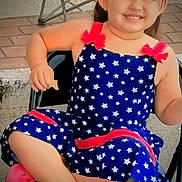 Amara is registered to the contest to win money with this photo: child, smiling, dress, stars, red_bows, pink_shoes, chair, outdoor, snack, happy, person, cute, young, sitting, pavement, footwear, playful, casual, daylight, relaxed