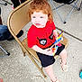 black_shorts, bracelet, casual_clothing, child, concrete_floor, curly_hair, cute, daylight, folding_chair, holding, legs, looking_up, outdoor, people, plastic_shoes, red_hair, seated, snack, spiderman_shirt, toddler