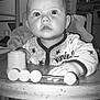 baby, black_and_white, child, closeup, curious, expression, face, furniture, hand, high_chair, indoor, infant, kitchen, pajamas, person, seatbelt, stars, table, toy, wood