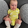 Maximillian is registered to the contest to win money with this photo: baby, infant, yellow_onesie, crab_print, socks, couch, gray_cushions, smile, cheeky_expression, seated, indoors, cute, child, person, apparel, soft_texture, home, cozy, legs, face