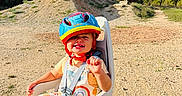 Léon a rejoint le concours — aidez-le/la à gagner de superbes lots ! bike_seat, blue_sky, child, colorful, daylight, dirt_path, happy, helmet, nature, outdoor, overalls, person, playful, safety_harness, seat, smiling, sunny, toddler, trees, young_child