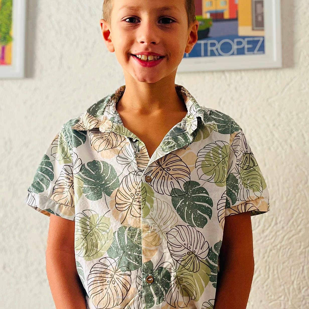 Louis a rejoint le concours — aidez-le/la à gagner de superbes lots ! child, boy, smiling, standing, shirt, patterned_clothing, tropical, leaf_pattern, indoor, wall, texture, framed_poster, colorful, portrait, happy, casual, short_hair, person, background, art