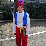 Louis a rejoint le concours — aidez-le/la à gagner de superbes lots ! child, costume, purple_feather, hat, smile, outdoor, sunny, fence, tree, pants, vest, white_shirt, shoes, playful, happy, person, standing, daylight, background, young