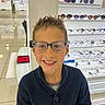 boy, casual, child, clothing, display_shelf, eyeglasses, eyewear, face, fashion, glasses, happy, indoor, person, portrait, retail, shopping, smiling, spiky_hair, store, young