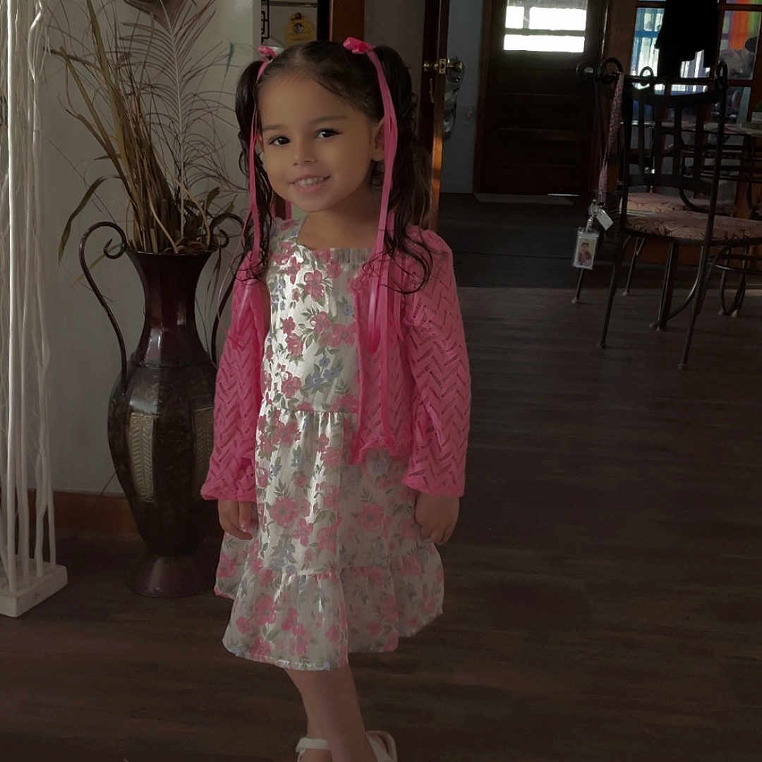 Willow is registered to the contest to win money with this photo: child, door, dress, floor, furniture, girl, hair, happy, home, indoor, light, person, pink_ribbons, plant, shoes, smile, standing, vase, window, wooden_floor