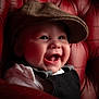 baby, black_outfit, cap, cheeks, child, closeup, clothing, cute, eyes, face, happy, hat, indoor, infant, laughing, leather_chair, portrait, red_chair, smiling, soft_lighting