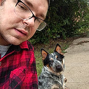 Oakley Lee joined the competition — help win amazing prizes! person, dog, selfie, outdoor, sidewalk, garden, trees, glasses, plaid_shirt, blue_heeler, australian_cattle_dog, black_white_coat, sitting, leash, portrait, close_up, pet, companion, daylight, humorous