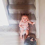 Alliyah joined the competition — help win amazing prizes! toddler, child, stairs, carpet, indoor, plush_toy, smiling, pigtails, cute, happy, person, clothing, shorts, top, wood_floor, wall, hand, toy, playful, home