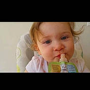 Karli Mae joined the competition — help win amazing prizes! child, toddler, face, food_pouch, high_chair, indoor, curly_hair, blue_eyes, drinking, baby, cute, infant, white_clothing, young_child, portrait, feeding, soft_lighting, closeup, healthy, happy