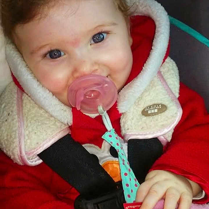Karli Mae joined the competition — help win amazing prizes! baby, blue_eyes, car_seat, child, closeup, cozy, curly_hair, cute, face, fleece_collar, hand, indoor, infant, pacifier, person, red_clothing, seatbelt, smiling, toy, warm_clothing