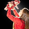 Chloe joined the competition — help win amazing prizes! baby, backlighting, black_background, child, dramatic_lighting, dress, family, family_bond, headband, holding, indoor, infant, lifting, long_hair, mother, parent, portrait, red_clothing, smiling, studio