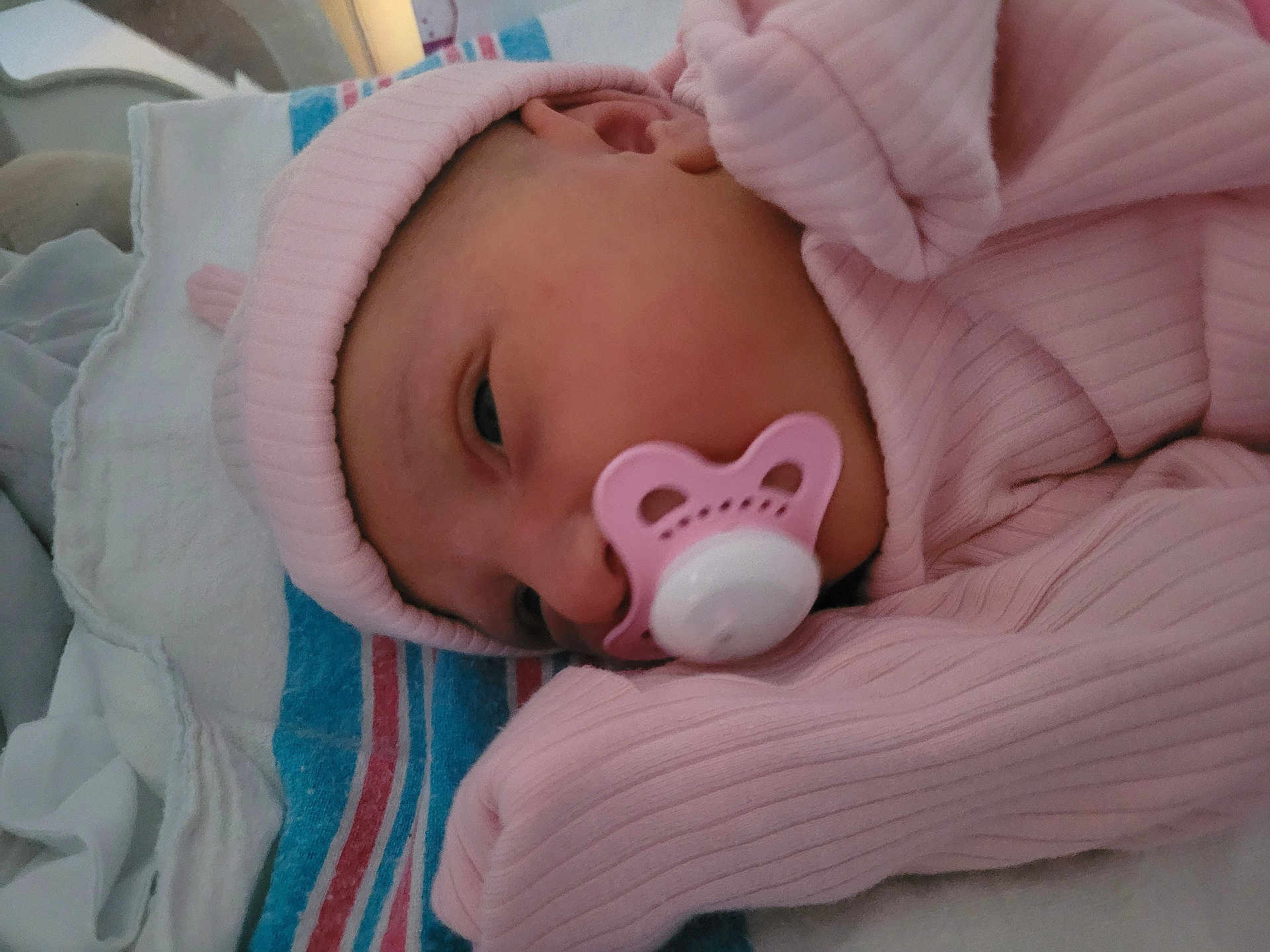 Amelia is registered to the contest to win money with this photo: newborn, baby, pacifier, pink_clothing, hat, blanket, sleeping, infant, closeup, face, soft_lighting, indoors, cute, resting, child, portrait, cozy, striped_blanket, early_morning, peaceful