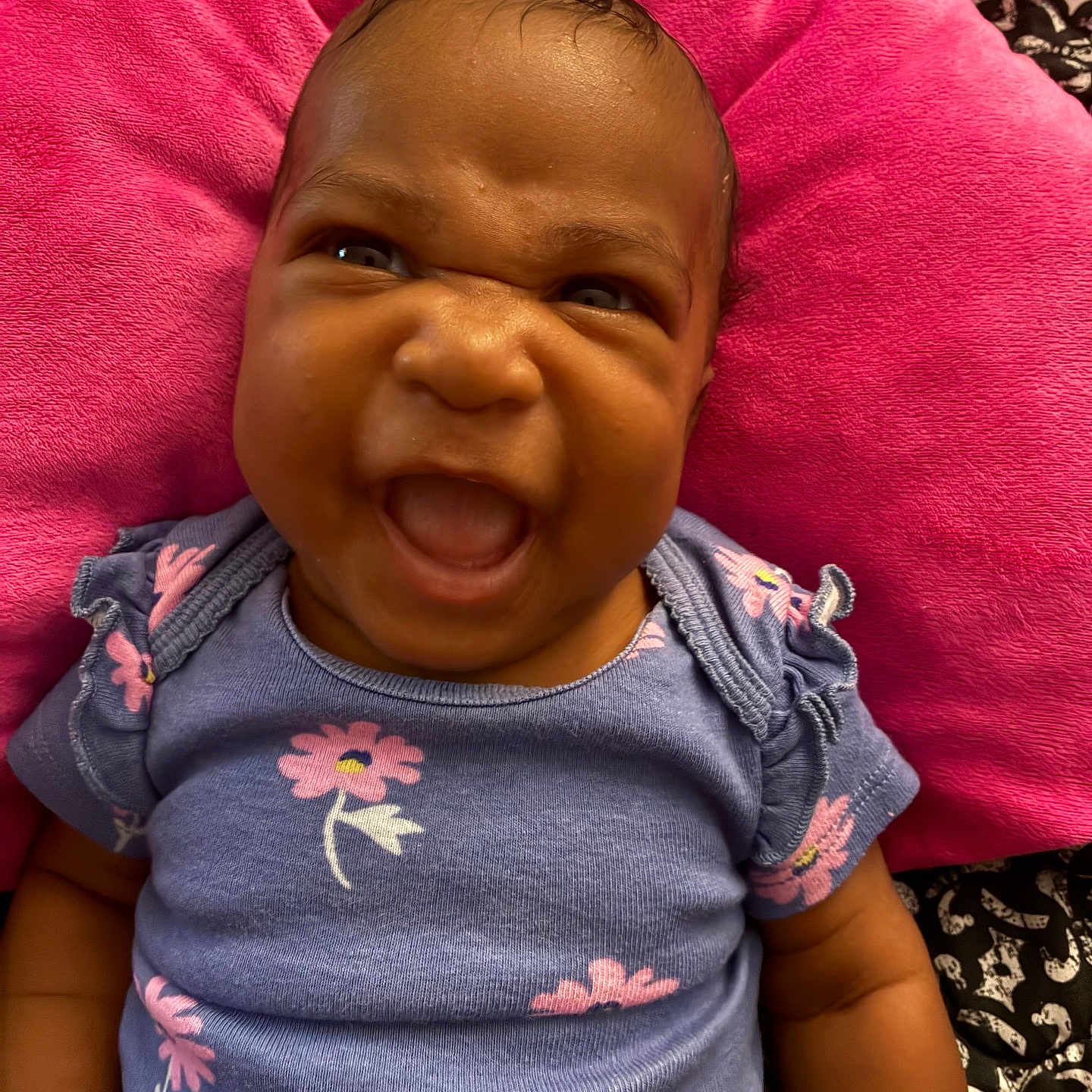Azaliah is registered to the contest to win money with this photo: baby, child, infant, smiling, purple_clothing, floral_pattern, cushion, pink, happy, face, portrait, cute, lying_down, indoors, skin, head, expression, person, baby_girl, closeup