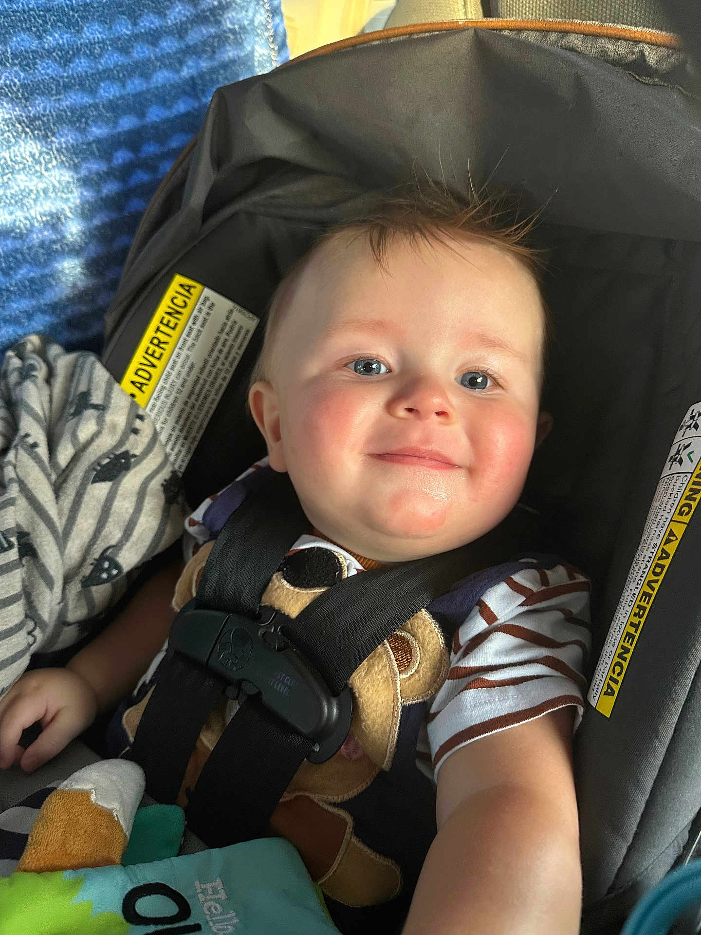 Kaysen is registered to the contest to win money with this photo: baby, child, car_seat, smile, blue_eyes, striped_shirt, blanket, toy, seatbelt, infant, close_up, indoors, cute, happy, young_child, soft_lighting, face, person, safety, comfort