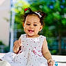 Neriah joined the competition — help win amazing prizes! toddler, child, smiling, outdoor, dress, white_dress, cherry_pattern, hair_clips, keys, pacifier, sitting, happy, sunlight, curly_hair, playful, nature, blurred_background, daylight, cute, person