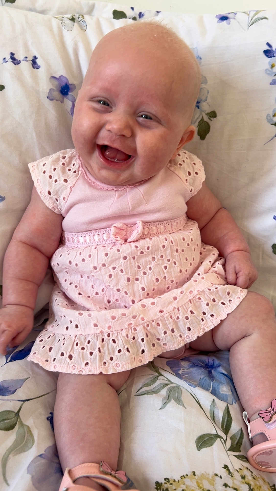 Aurelia is registered to the contest to win money with this photo: baby, infant, smiling, pink_dress, sitting, happy, cute, child, face, skin, footwear, shoe, flower_pattern, cushion, indoors, portrait, cheerful, young, people, human