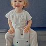 toddler, child, smiling, indoor, potty_chair, bunny_shape, white_shirt, pants, sandals, hair_bun, floor, couch, happy, cute, childhood, playful, toys, home, furniture, portrait