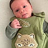 baby, infant, child, green_clothing, embroidered_animal, cute, lying_down, soft_surface, alert, hand, face, portrait, young_child, text_on_clothing, cozy, indoors, expression, skin, eyes, head