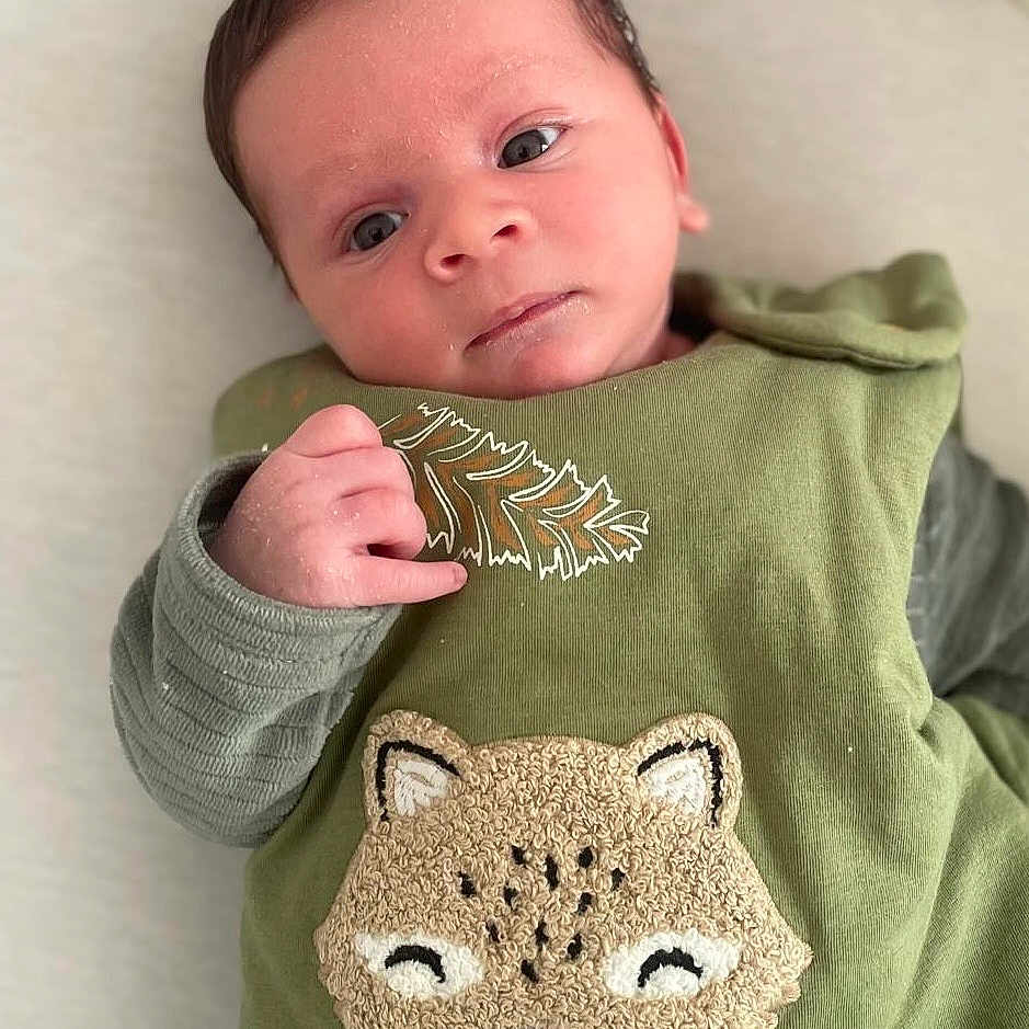 Noah a rejoint le concours — aidez-le/la à gagner de superbes lots ! baby, infant, child, green_clothing, embroidered_animal, cute, lying_down, soft_surface, alert, hand, face, portrait, young_child, text_on_clothing, cozy, indoors, expression, skin, eyes, head