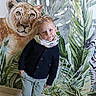 Eden a rejoint le concours — aidez-le/la à gagner de superbes lots ! child, boy, portrait, indoor, wall_mural, jungle_theme, lioness_painting, greenery, scarf, sweater, pants, tiles, casual_pose, blond_hair, playful, smile, face, person, background, artwork