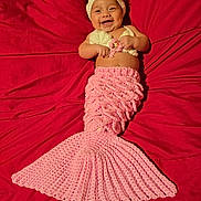 Andrea is registered to the contest to win money with this photo: baby, smiling, crocheted, mermaid, pink, headband, blanket, red, cute, infant, happy, costume, handmade, portrait, lying_down, child, toddler, knitwear, cozy, playful