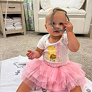 Lauren joined the competition — help win amazing prizes! toddler, child, pink_tutu, white_onesie, blanket, carpet, living_room, curtain, furniture, cabinet, toy, face, hand, foot, sitting, playful, indoors, cute, baby, person