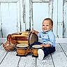 baby, child, toddler, smiling, happy, portrait, musical_instruments, drums, percussion, bongo_drums, djembe, wooden_instruments, sitting, blue_shirt, bow_tie, dark_pants, shoes, indoors, rustic_background, photography