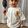 Matteo is registered to the contest to win money with this photo: toddler, child, face, portrait, hairbrush, brush, white_tshirt, teddy_print, curtain, hardwood_floor, cargo_pants, sock, standing, indoor, eyes, hands, smile, toy, clothing, floor