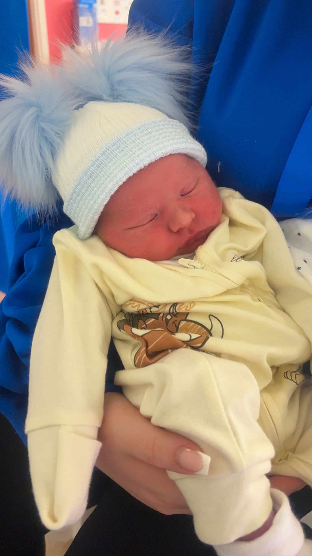 Tommy is registered to the contest to win money with this photo: newborn, baby, hat, pom_pom, sleeping, infant, clothing, person, hand, holding, cute, cozy, soft, warm, indoor, portrait, peaceful, closeup, child, resting
