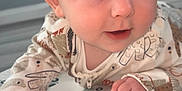 Tommy is registered to the contest to win money with this photo: baby, child, infant, face, blue_eyes, onesie, animal_print, hand, floor, mat, pattern, car_pattern, cute, curious, indoor, portrait, young_child, skin, head, expression