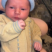 Tommy joined the competition — help win amazing prizes! baby, infant, knitwear, hat, pom_pom, yellow_clothing, blue_hat, hand, face, person, sitting, close_up, cute, indoor, soft_texture, warm_clothing, portrait, newborn, skin, curious