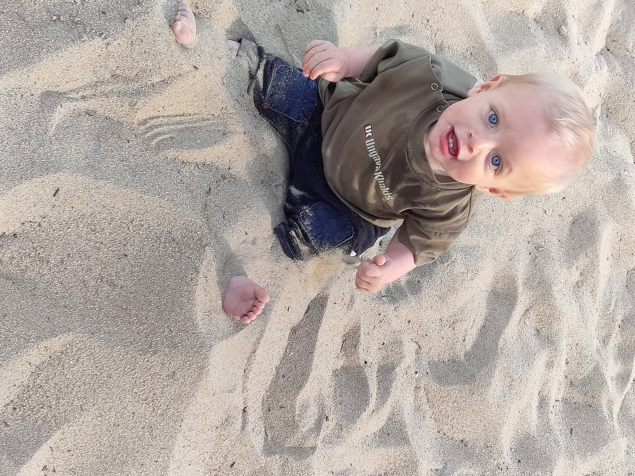 Jakob participe au concours pour gagner de l'argent avec cette photo : baby, baby_toddler_clothing, beach, child, comfort, flooring, fun, gesture, grass, landscape, people_in_nature, person, play, recreation, sand, shadow, smile, soil, toddler