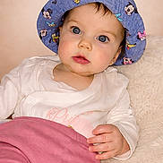 Rose participe au concours pour gagner de l'argent avec cette photo : baby, child, blue_hat, cartoon_characters, white_top, pink_pants, soft_background, curious_expression, portrait, indoor, cute, infant, person, face, hand, clothing, closeup, sitting, young_child, hat