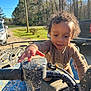 Marcus joined the competition — help win amazing prizes! child, toddler, curly_hair, outdoor, sunny, atv, muddy, blue, handlebar, vehicle, nature, trees, grass, car, pickup_truck, road, person, play, curious, daytime