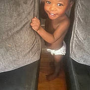 Zarie joined the competition — help win amazing prizes! toddler, child, smiling, indoor, cushion, gray, wooden_floor, barefoot, diaper, happy, person, face, baby, cute, holding, standing, small_hand, playful, young_child, furniture