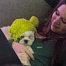puppy, dog, person, hat, yellow_hat, indoor, couch, holding, cute, sleepy, warm, cozy, pet, fur, face, hand, smile, comfort, relaxation, portrait